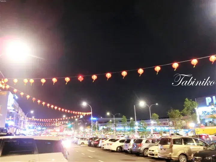 赤い提灯と駐車された車で飾られた通りの夜景。タビニコの透かし文字あり。