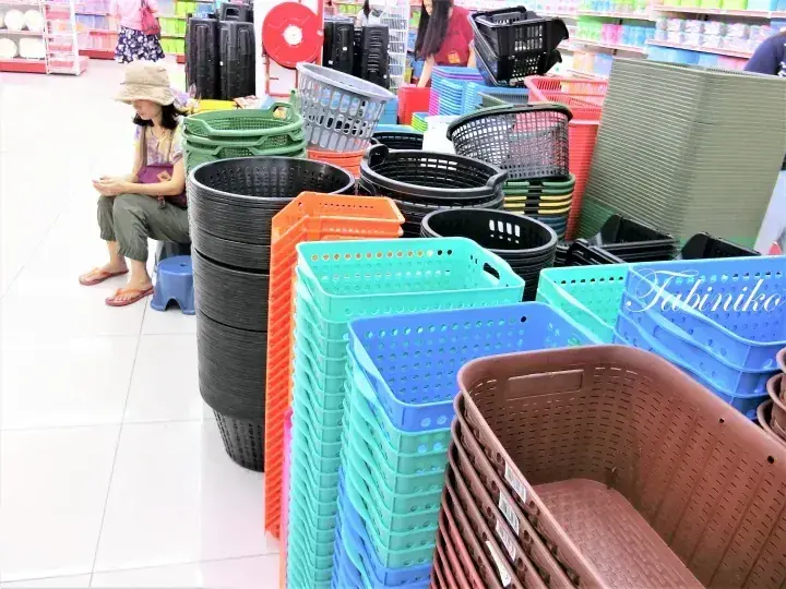Stacks of colorful plastic storage baskets and bins in a store aisle with a woman sitting nearby.
