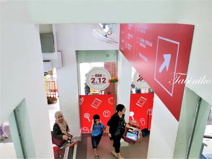 赤い看板と「RM 2.12」の価格表示があり、Tabinikoの透かしが入った施設入口での訪問者の様子。