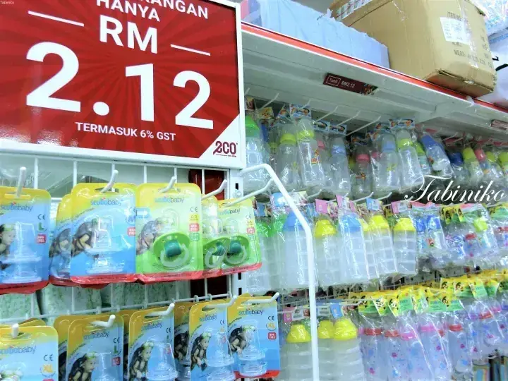 Shelves of baby bottles and pacifiers at a 2CO store with a red price sign showing RM 2.12 including 6% GST.