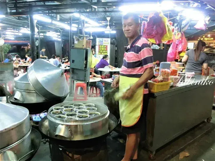 Street vendor preparing traditional Malaysian kueh in a bustling night market stall.