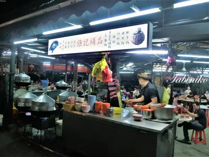 A bustling night food stall named Qiang Ji Bu Pin serving traditional soups in a Malaysian hawker center.