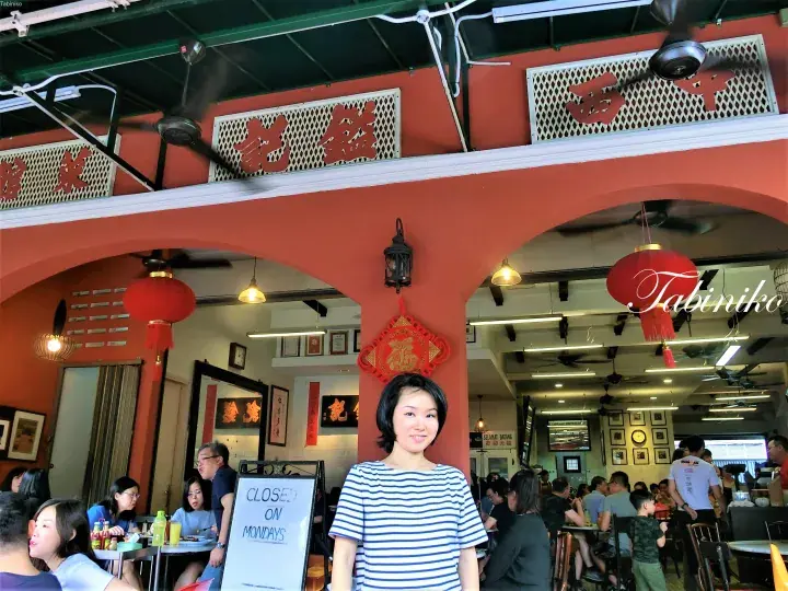 A woman stands in front of a traditional Chinese restaurant entrance with red lanterns and ceiling fans.