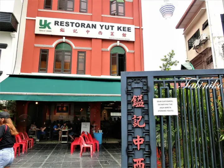 The red facade of Restoran Yut Kee with its green awning and outdoor seating area.