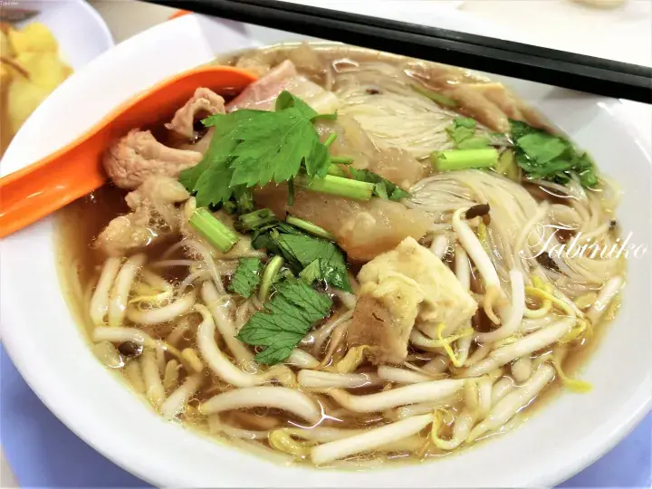 A bowl of Malaysian mee soto with rice noodles, chicken, bean sprouts, and herbs in a savory broth.