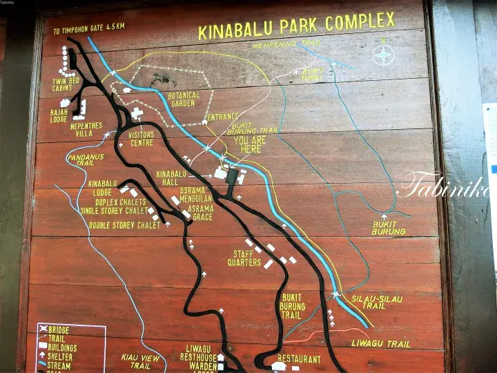 Wooden map of Kinabalu Park Complex showing trails, lodges, and the entrance near the river.
