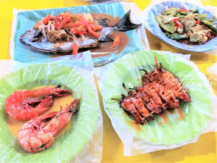 Assam fish, grilled prawns, grilled squid, and stir-fried vegetables served on banana leaves at a Malaysian restaurant.