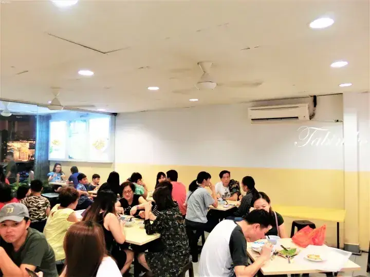 Busy dining hall with patrons eating at tables under ceiling fans and air conditioning in a local Malaysian restaurant.