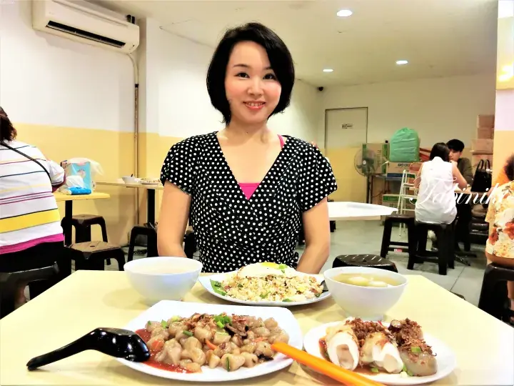 マレーシアの料理が並ぶテーブルで笑顔を見せる女性。揚げ飯やチキンライス、スープなどが食べられるローカルフード店。