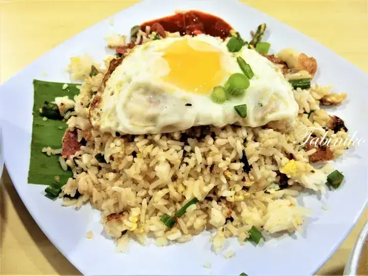 Nasi Goreng Kampung with a sunny-side-up egg, sambal, and green onions served on a white plate.