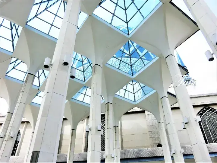 Low angle view of the National Mosque of Malaysia’s white pillars and geometric glass roof.