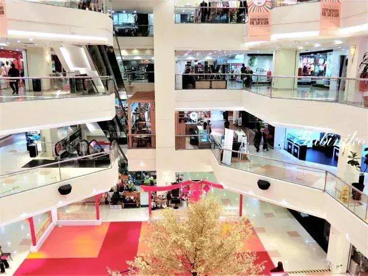 Multi-level shopping mall atrium with escalators, glass railings, and a golden decorative tree in the center.
