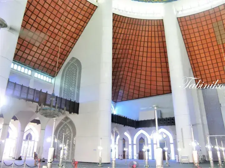 Interior of Masjid Wilayah Persekutuan featuring towering white pillars and a distinctive terracotta-tiled ceiling.
