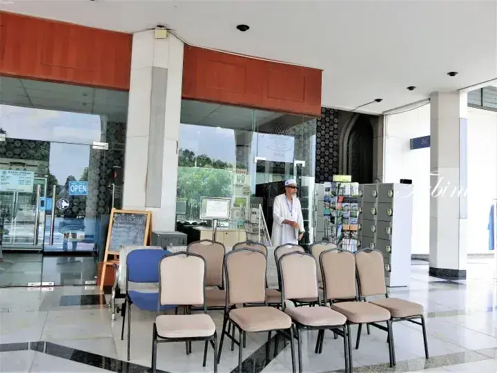 Rows of beige chairs in a modern lobby with glass doors and a staff member standing near a brochure rack.
