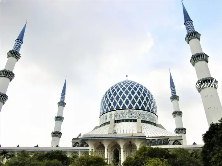 Blue Mosque Shah Alam featuring its iconic blue dome and four towering minarets against a cloudy sky.