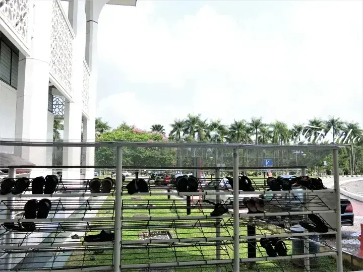 Shoe racks outside a mosque with white architectural details and palm trees in the background.