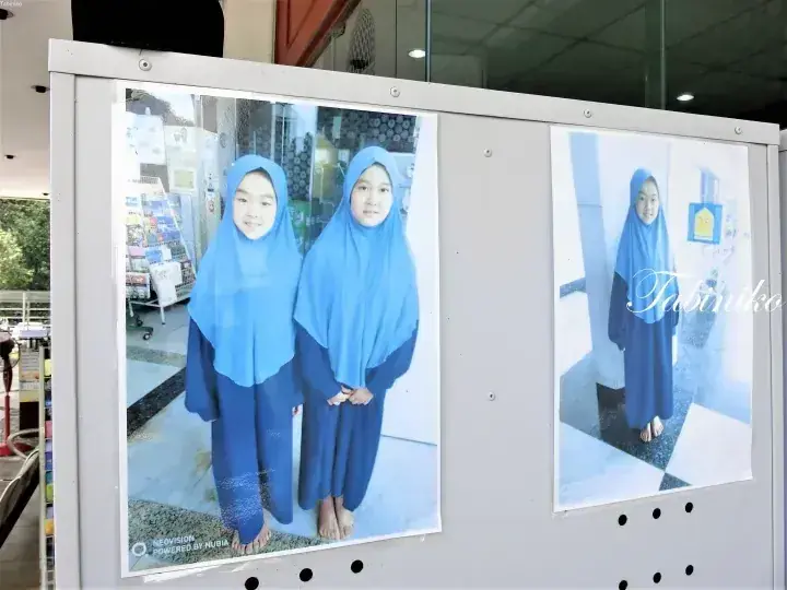Two young girls in blue hijabs and matching outfits standing together, displayed on a white board next to a solo portrait.