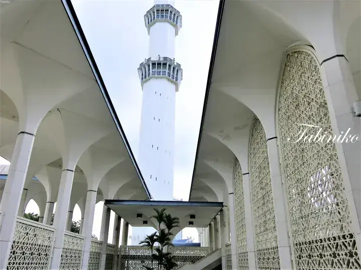 View of the white minaret and arched colonnades of a mosque featuring intricate geometric lattice walls.
