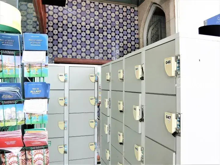 Grey numbered lockers and brochures in a building with patterned tiles and an arched window.