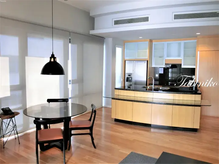 Modern kitchen with light wood cabinetry and black granite island, adjacent to a dining area with a round glass table and black pendant light.