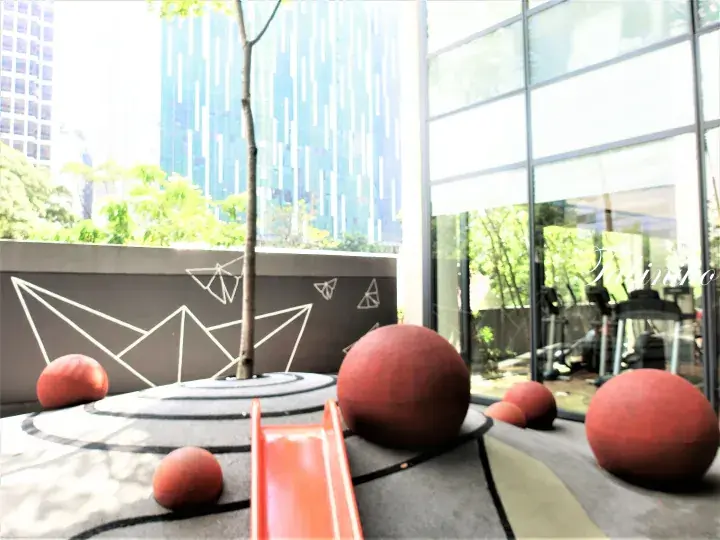 Modern playground with red spheres and a slide on a rooftop terrace overlooking Kuala Lumpur skyscrapers.