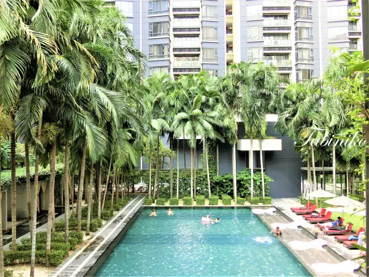 Swimmers enjoy a long pool surrounded by tall palm trees at a modern residential complex in Malaysia.