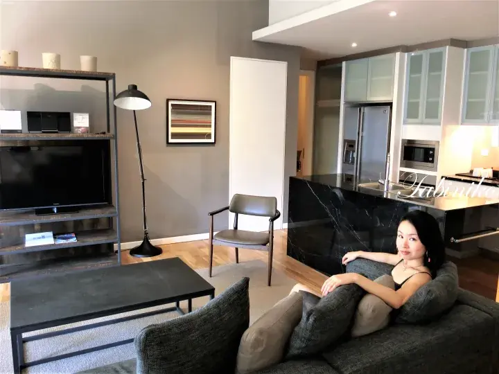 Woman relaxing on a sofa in a modern apartment living room with a kitchen island and TV stand.