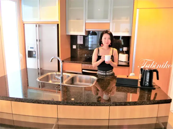 Woman holding a cup in a modern kitchen with granite countertops and stainless steel appliances.