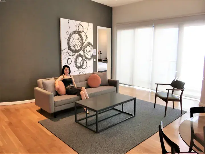 Woman relaxing on a sofa in a modern apartment living room with a large abstract painting and glass doors.