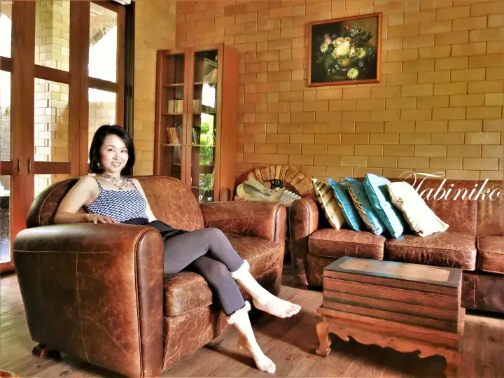 A woman relaxing on a brown leather sofa in a rustic room with brick walls and wooden furniture.