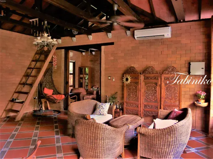 Cozy living room with wicker furniture, brick walls, and a wooden staircase at Tabiniko.