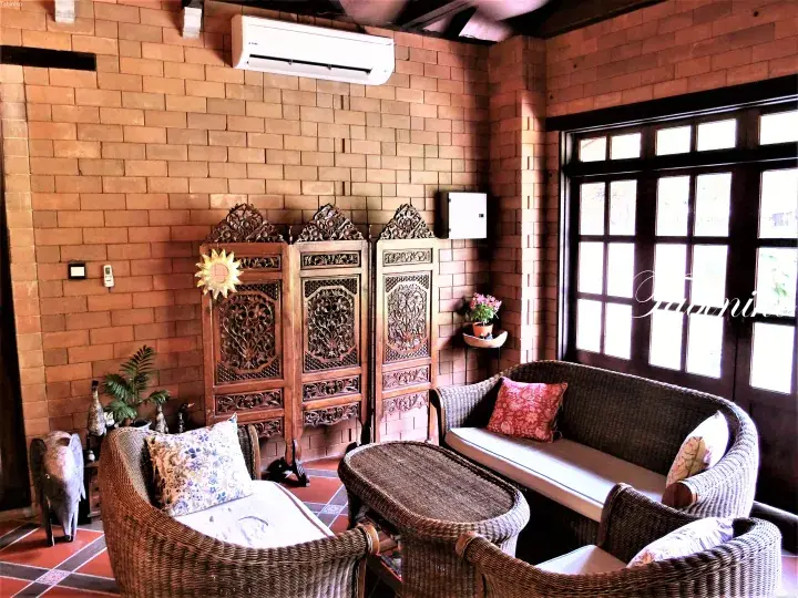 Cozy wicker furniture arrangement in a room with exposed brick walls and ornate wooden screens.
