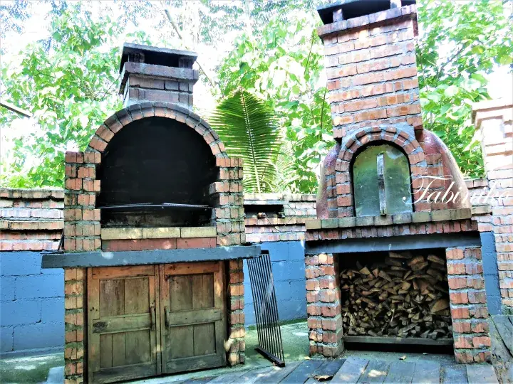 Traditional brick barbecue ovens with chimneys and wood storage at an outdoor property in Malaysia.