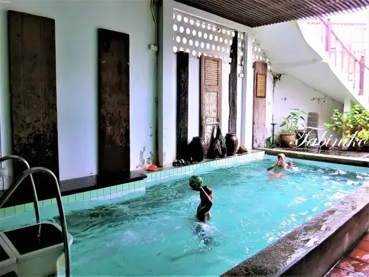 Children playing in the swimming pool at Dabinho, featuring rustic wooden doors and decorative pottery along the tiled edge.