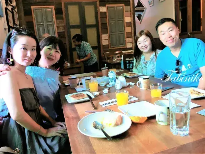 Four smiling guests enjoying breakfast at a rustic wooden table in a cozy restaurant.