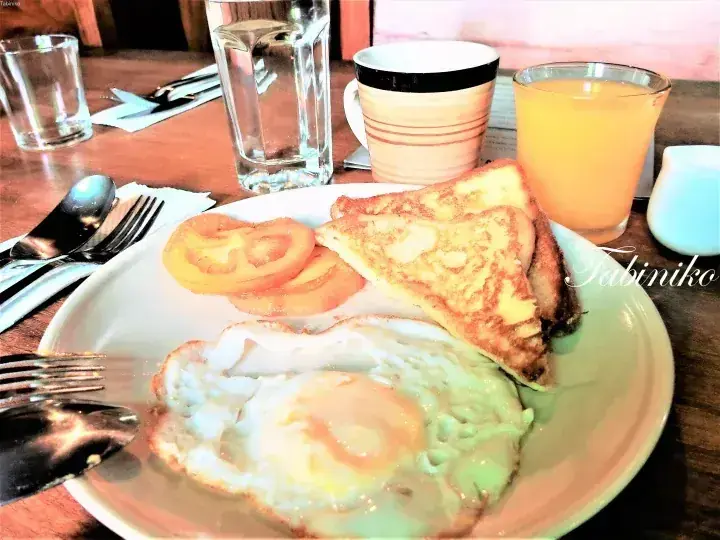 A hearty breakfast plate with fried eggs, toast, and tomato slices, accompanied by orange juice and coffee.
