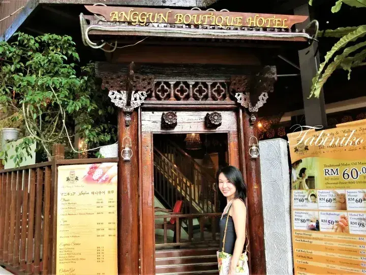 Woman standing at the ornate wooden entrance of Anggun Boutique Hotel with spa menus displayed nearby.