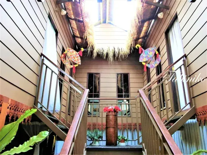 Wooden staircase with metal railings leading to a balcony, decorated with colorful fabric ornaments and a thatched roof overhang.