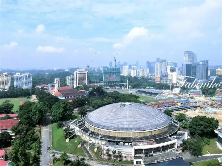 Aerial view of the Axiata Arena in Kuala Lumpur with the city skyline and construction sites in the background.