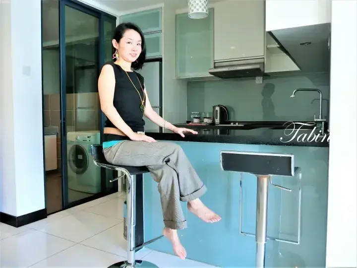 A woman sits on a bar stool in a modern kitchen with a blue island counter and glass sliding doors.