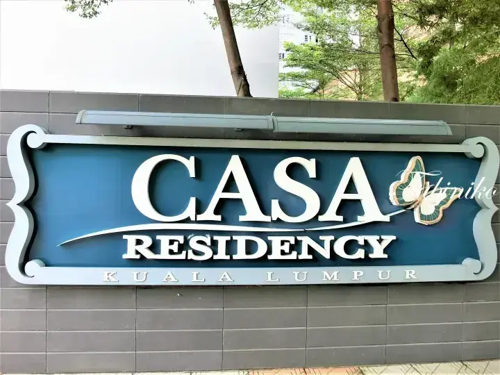 Blue signboard displaying Casa Residency Kuala Lumpur with a butterfly logo mounted on a grey tiled wall.