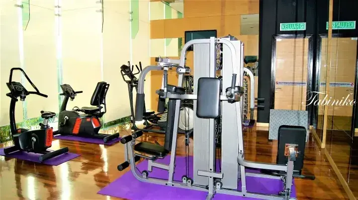 Modern gym interior at Tabinka featuring weight machines, exercise bikes, and purple mats on polished wood flooring.
