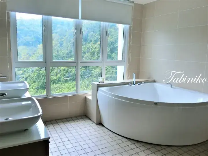 Spacious bathroom with a large white bathtub and dual sinks, featuring a window with a view of lush green hills.