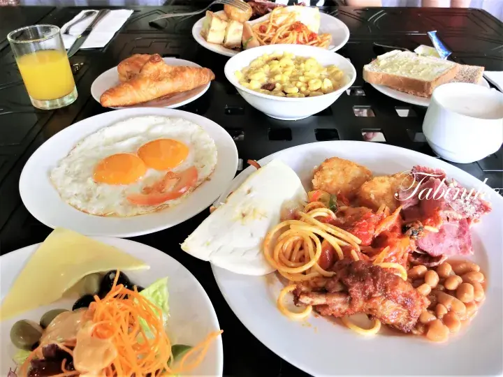 卵、パスタ、クロワッサン、新鮮なジュースが並ぶ豪華な朝食ビュッフェのテーブル。