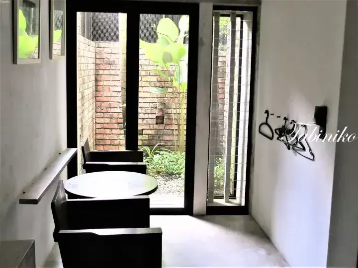 Modern dining area with a round table and black chairs overlooking a brick-walled courtyard with greenery.