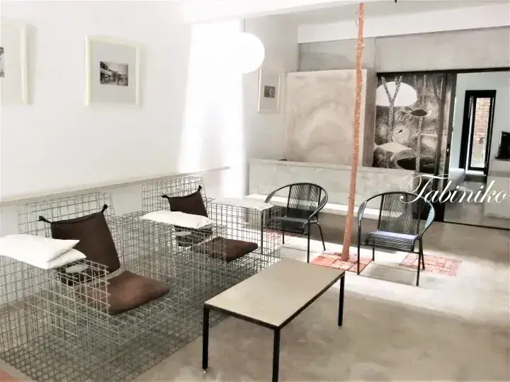 Modern interior with wire mesh seating, black chairs, and a wooden pole in a bright space featuring Tabiniko branding.