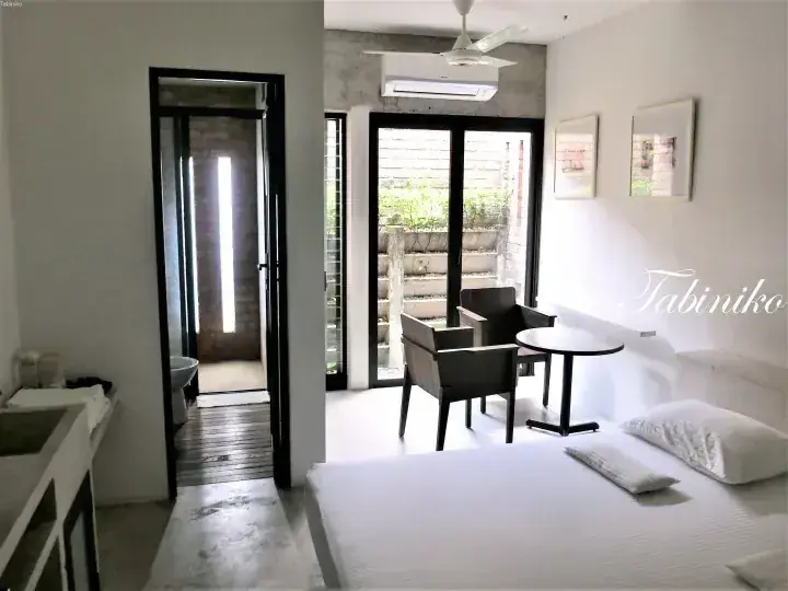 Modern bedroom with white linens, seating area, and glass doors leading to a patio at Tabiniko.