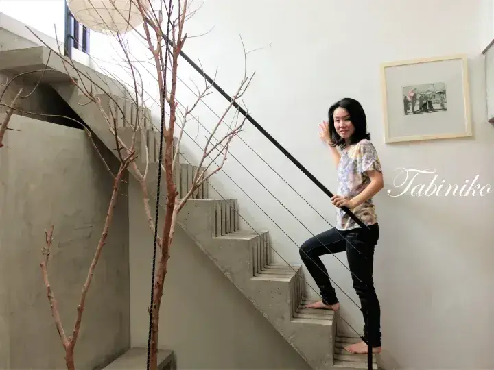 Woman posing on a modern concrete staircase with a decorative bare tree branch in a minimalist interior.