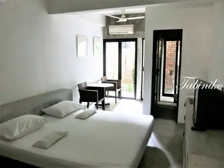 Modern hotel room with a double bed, seating area, and glass doors leading to a balcony.