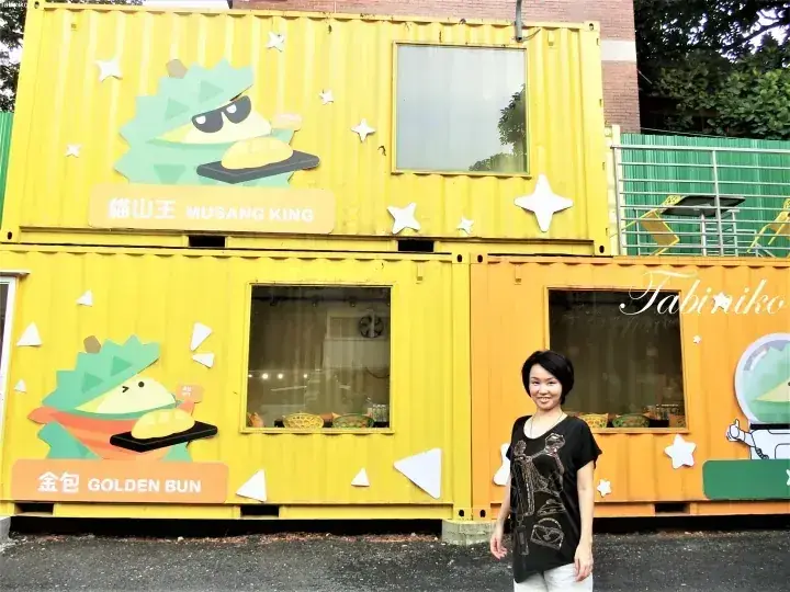 A woman stands in front of a yellow container shop featuring Musang King and Golden Bun signage.